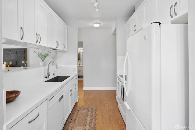 kitchen with white cabinets, a sink, white appliances, light countertops, and light wood-style flooring