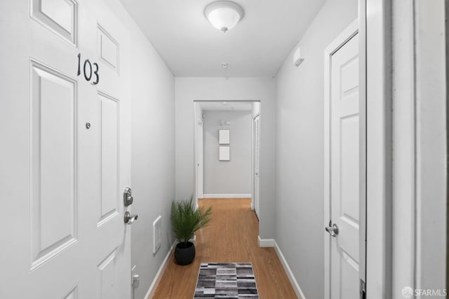 corridor featuring baseboards, visible vents, and light wood finished floors