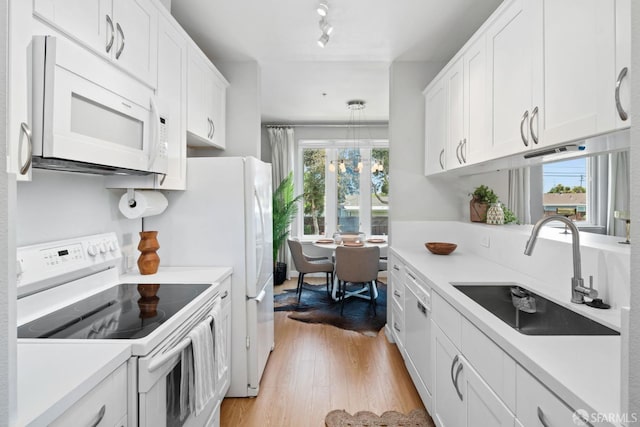 kitchen with a sink, light countertops, white appliances, and white cabinetry