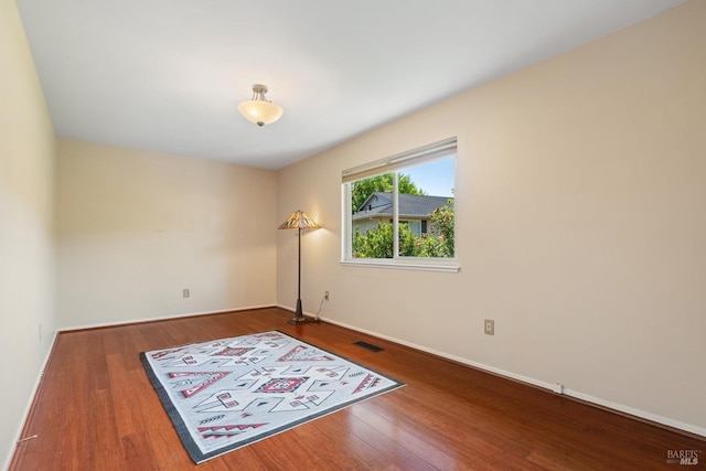 unfurnished room with baseboards, wood finished floors, and visible vents