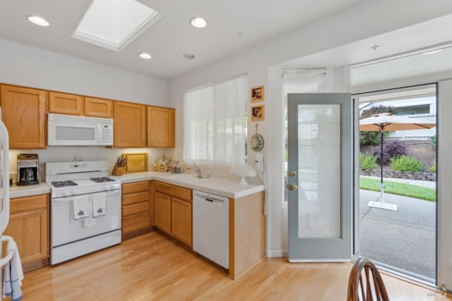 kitchen featuring a sink, white appliances, tile counters, and light wood-style floors