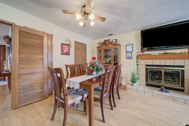 dining space featuring a tile fireplace, a ceiling fan, visible vents, baseboards, and light wood-style floors