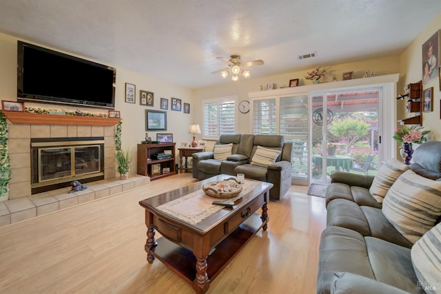 living room featuring a ceiling fan, a tile fireplace, visible vents, and wood finished floors