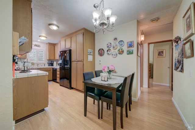 kitchen with light wood finished floors, tile countertops, black appliances, and a notable chandelier