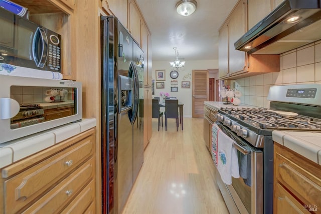 kitchen with under cabinet range hood, gas stove, tile counters, and black refrigerator with ice dispenser