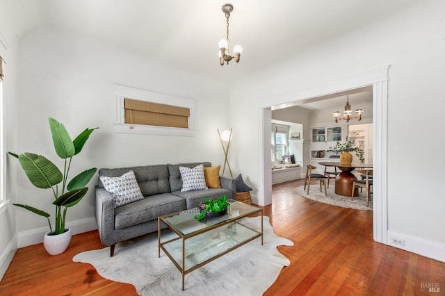 living area featuring vaulted ceiling, a chandelier, wood finished floors, and baseboards