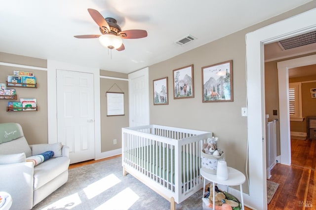 bedroom featuring a nursery area, visible vents, wood finished floors, and baseboards