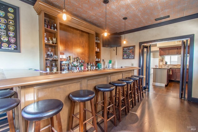 bar featuring a community bar, pendant lighting, an ornate ceiling, ornamental molding, and dark wood-style floors