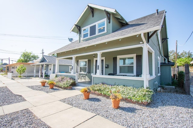 view of front of home featuring roof with shingles, covered porch, and fence