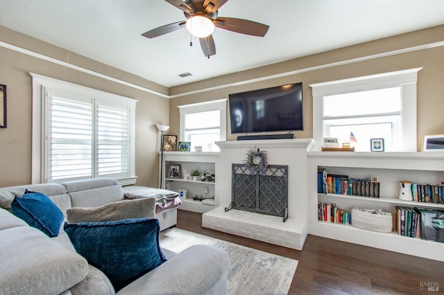 living room featuring a brick fireplace, a ceiling fan, visible vents, and wood finished floors