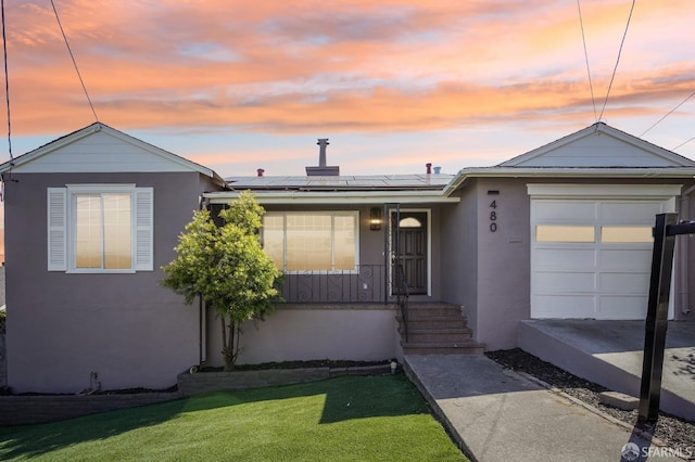 ranch-style house with stucco siding, roof mounted solar panels, a yard, a garage, and a porch