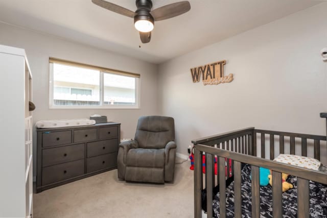 carpeted bedroom featuring a nursery area and a ceiling fan