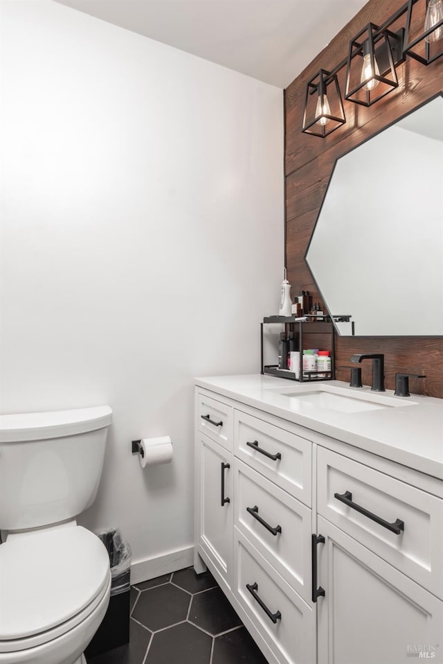 half bathroom with vanity, toilet, baseboards, and tile patterned floors