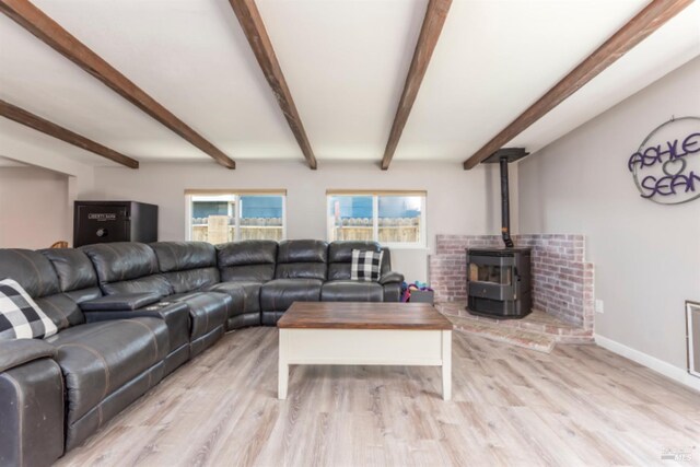 living area with a wood stove, beamed ceiling, baseboards, and light wood-style floors