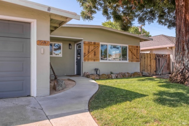 doorway to property featuring stucco siding, a gate, fence, and a lawn