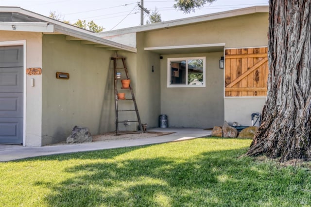 view of exterior entry with stucco siding and a lawn