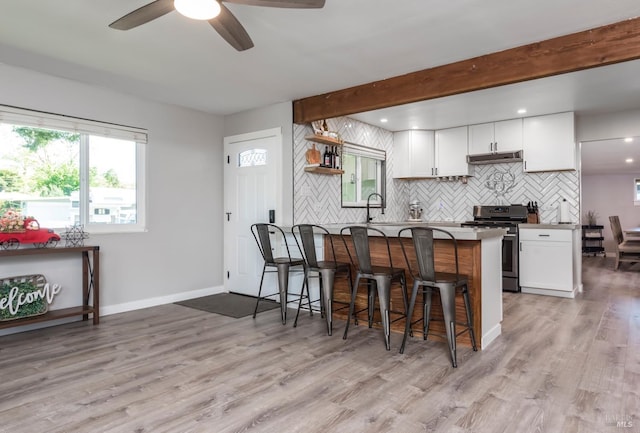 kitchen featuring stainless steel range with gas cooktop, a kitchen breakfast bar, white cabinetry, and under cabinet range hood