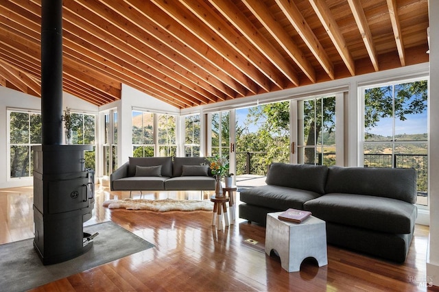 sunroom with lofted ceiling with beams, a healthy amount of sunlight, a wood stove, and wooden ceiling