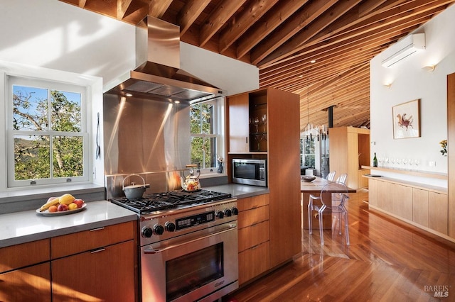 kitchen with a wall mounted air conditioner, a wealth of natural light, wall chimney exhaust hood, and appliances with stainless steel finishes