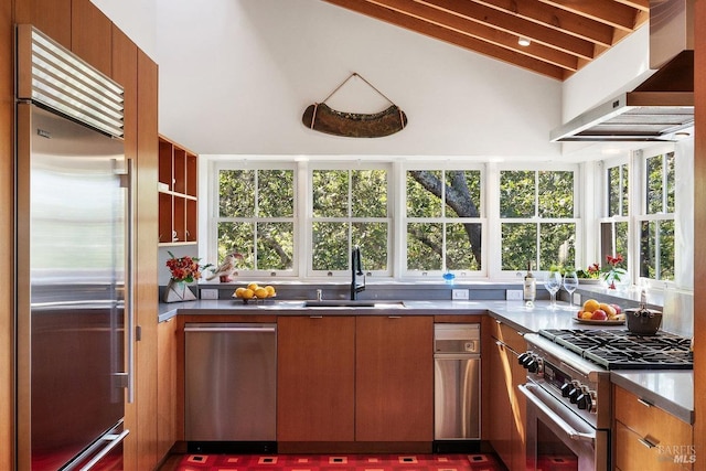 kitchen with high end appliances, under cabinet range hood, brown cabinetry, and a sink