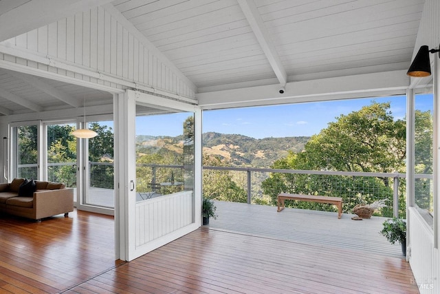 sunroom / solarium with a wealth of natural light, hardwood / wood-style floors, a mountain view, and vaulted ceiling with beams