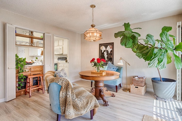 dining room featuring baseboards, a notable chandelier, light wood finished floors, and a textured ceiling
