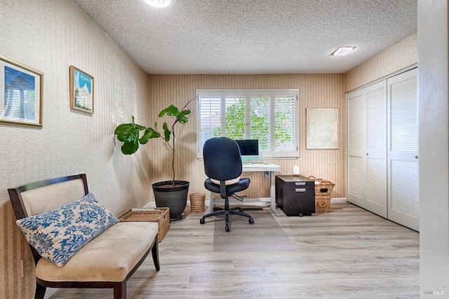 home office with wallpapered walls, a textured ceiling, wood finished floors, and baseboards