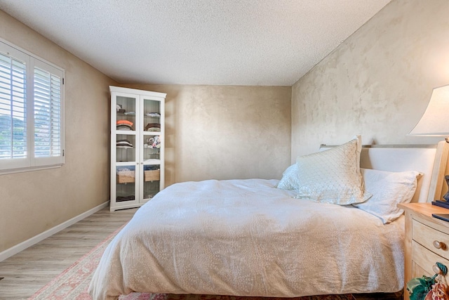 bedroom with a textured ceiling, light wood-style flooring, and baseboards
