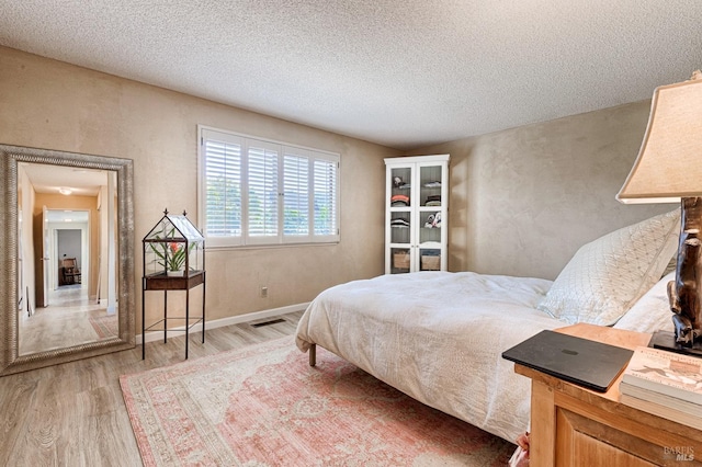bedroom with visible vents, a textured ceiling, and wood finished floors