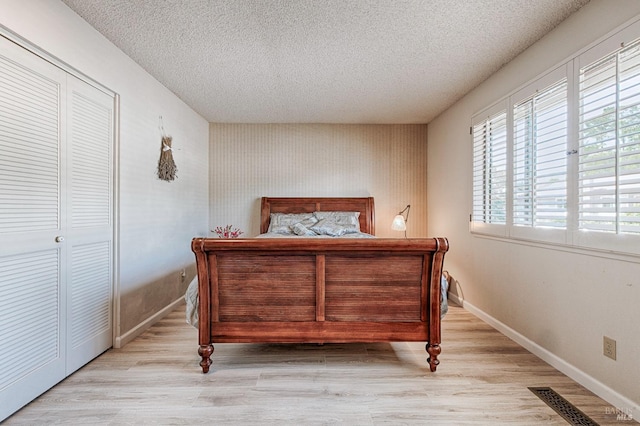 bedroom with a textured ceiling, baseboards, visible vents, and wood finished floors