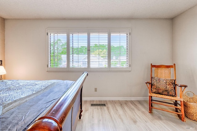 bedroom with a textured ceiling, baseboards, visible vents, and wood finished floors