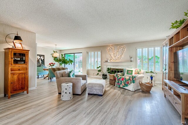 living room featuring a textured ceiling, light wood-style flooring, baseboards, and a brick fireplace