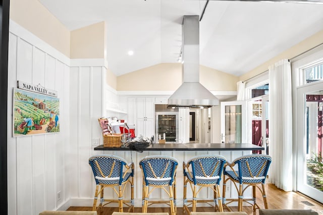 kitchen with a peninsula, lofted ceiling, light wood-style flooring, island range hood, and dark countertops