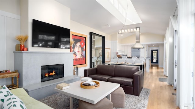 living area featuring vaulted ceiling, a glass covered fireplace, and light wood-style floors