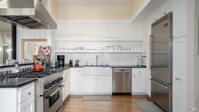 kitchen featuring a sink, exhaust hood, decorative backsplash, high quality appliances, and dark countertops