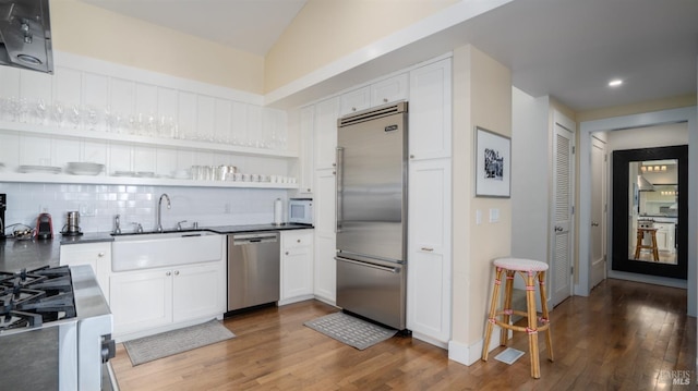 kitchen featuring wood finished floors, dark countertops, stainless steel appliances, white cabinets, and backsplash