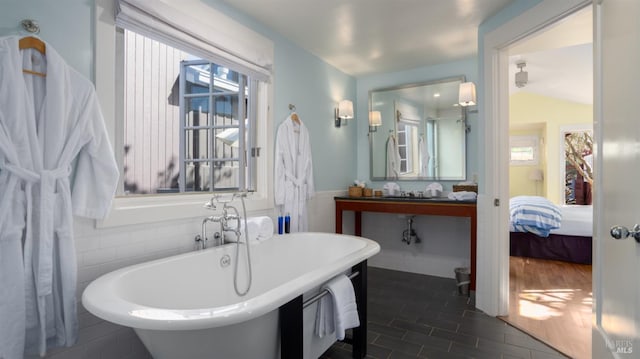 ensuite bathroom with tile walls, a soaking tub, connected bathroom, and a wainscoted wall
