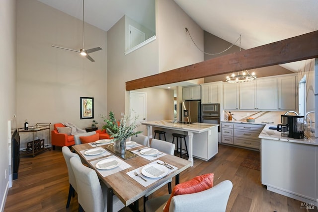 dining room with dark wood finished floors, ceiling fan with notable chandelier, and high vaulted ceiling