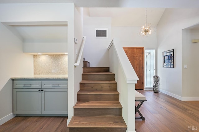 stairway featuring baseboards, a chandelier, visible vents, and wood finished floors