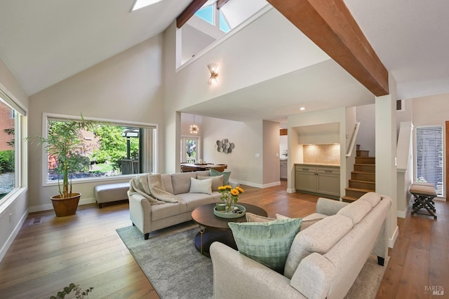 living area with baseboards, visible vents, high vaulted ceiling, hardwood / wood-style flooring, and stairway
