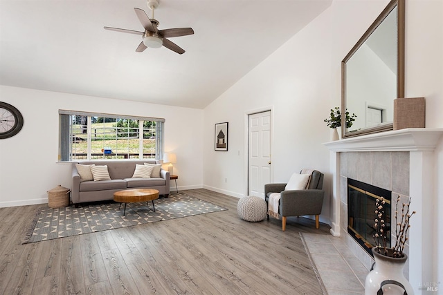 living area featuring a ceiling fan, a tile fireplace, baseboards, and wood finished floors