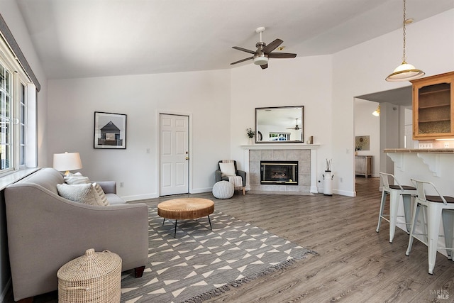 living room with a ceiling fan, baseboards, a tiled fireplace, and wood finished floors