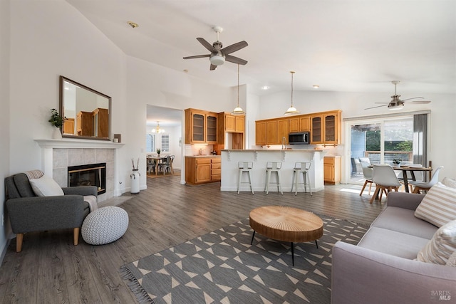 living room featuring ceiling fan, high vaulted ceiling, a tiled fireplace, and dark wood finished floors