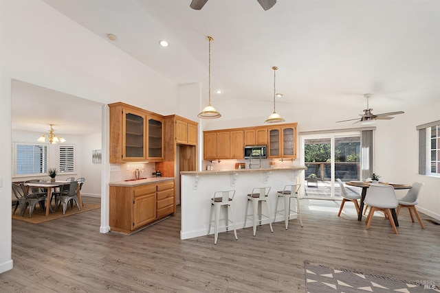 kitchen with light countertops, glass insert cabinets, stainless steel microwave, and ceiling fan with notable chandelier