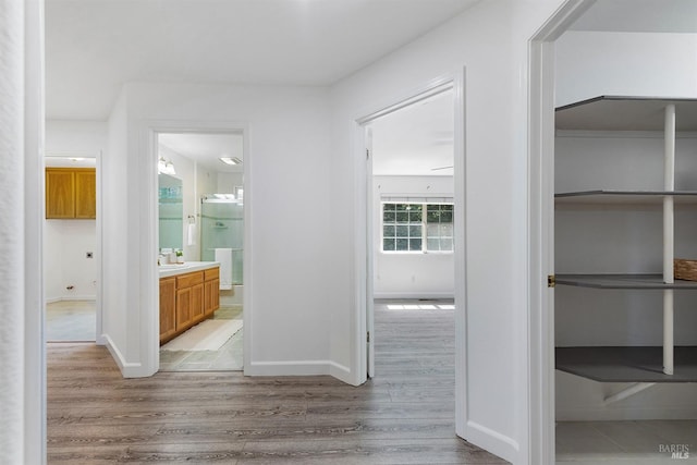 hall featuring baseboards, light wood-style floors, and a sink