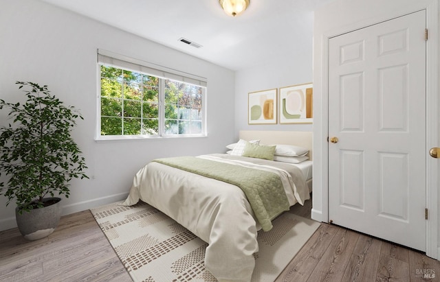 bedroom with baseboards, visible vents, and wood finished floors