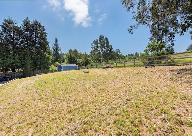 view of yard with a rural view, an outdoor structure, fence, and a shed