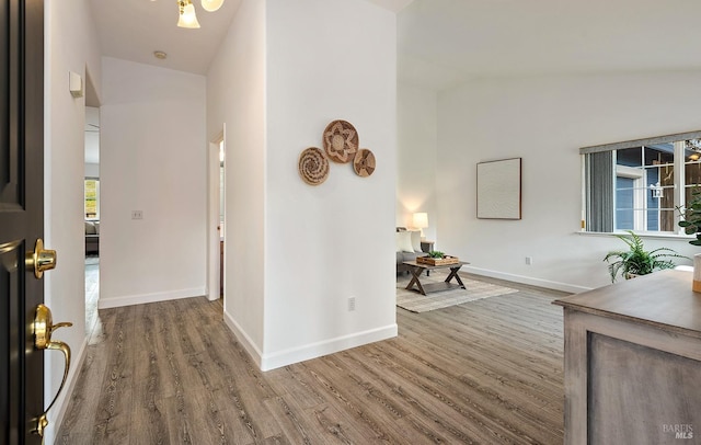 hallway featuring baseboards, wood finished floors, and lofted ceiling