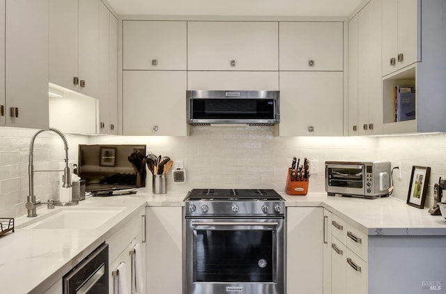 kitchen with a sink, a toaster, stainless steel appliances, white cabinets, and backsplash