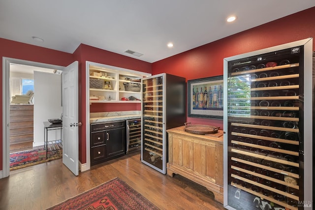 wine room featuring dark wood finished floors, visible vents, and beverage cooler